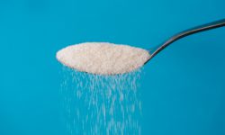 Studio picture of a metal spoon pouring sugar isolated on a blue background in cooking sweet sugar addiction unhealthy diet overweight and obesity concept